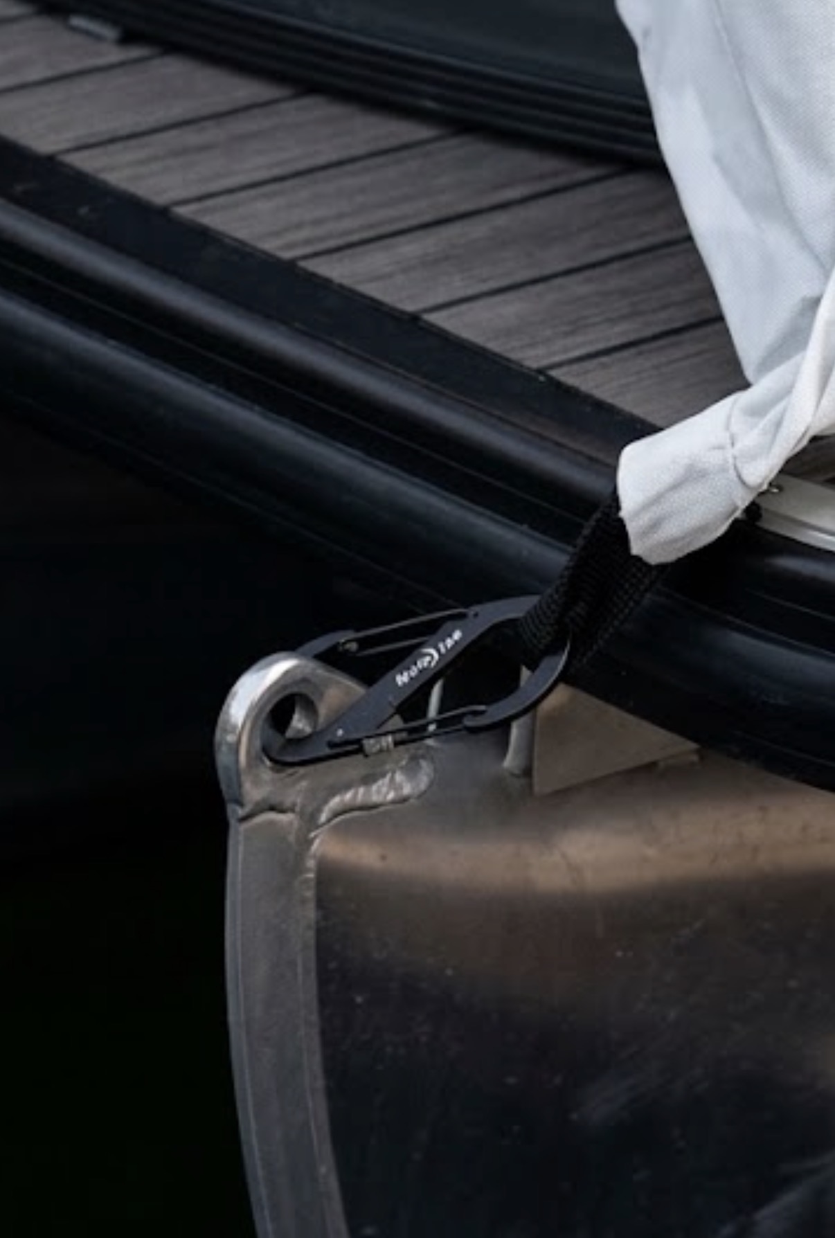 Black locking carabiner connecting a white boat cover strap to the front of a pontoon
