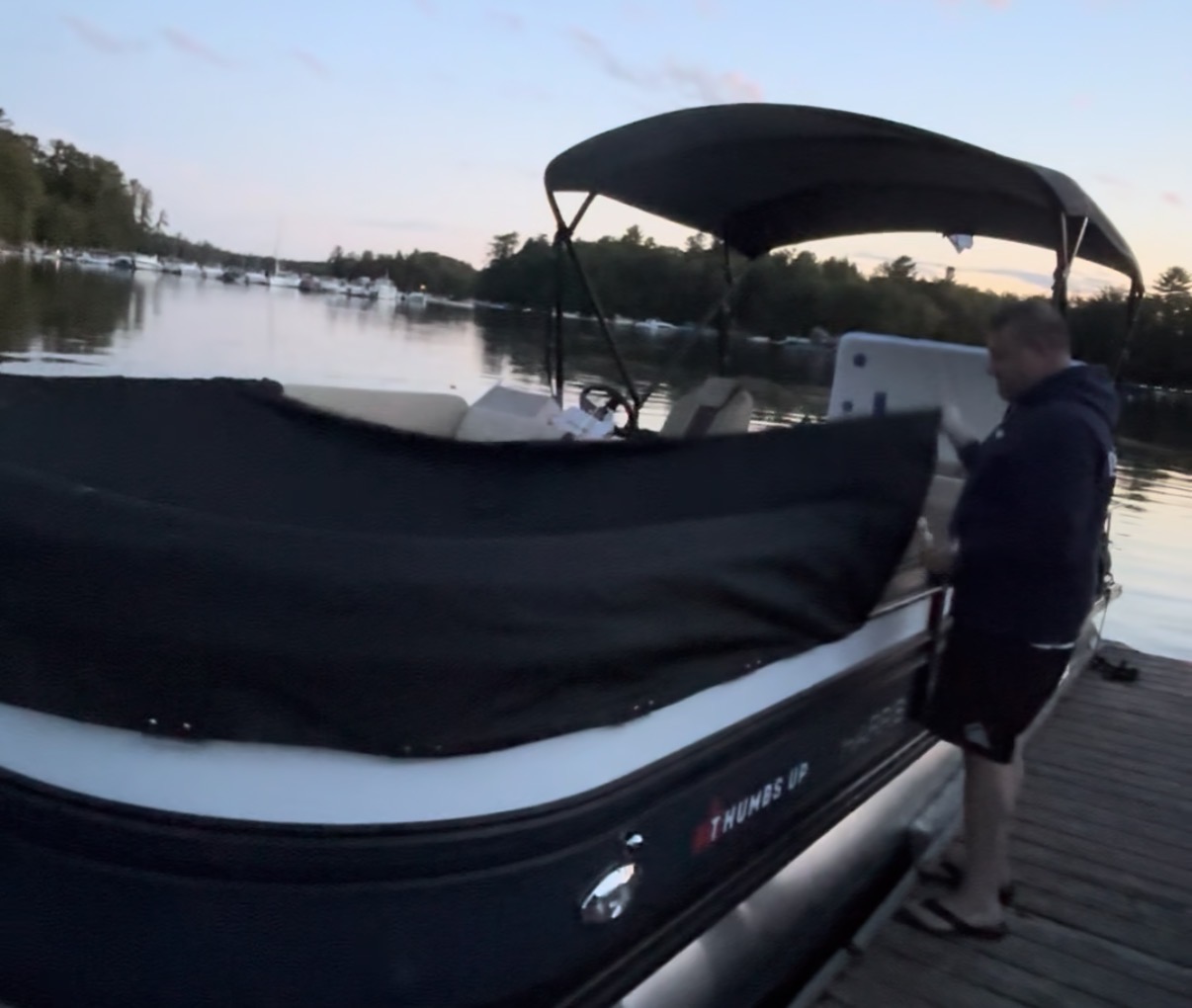 Boater installing a black heavyweight snapped pontoon cover at dusk